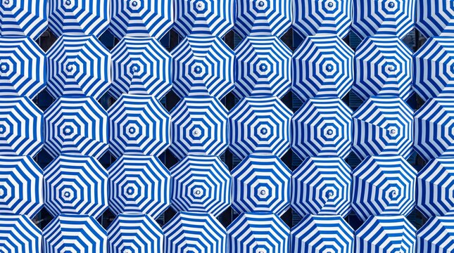 Aerial top view of numerous identical blue and white striped beach umbrellas arranged neatly in a geometric pattern on a sunny summer resort seashore.