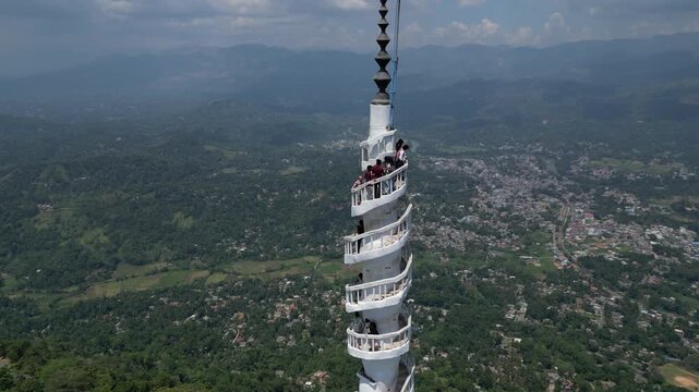 Aerial view of the spiraling Ambuluwawa Tower with people on the observation decks, surrounded by lush green hills and the town of Gampola, Central Province, Sri Lanka.