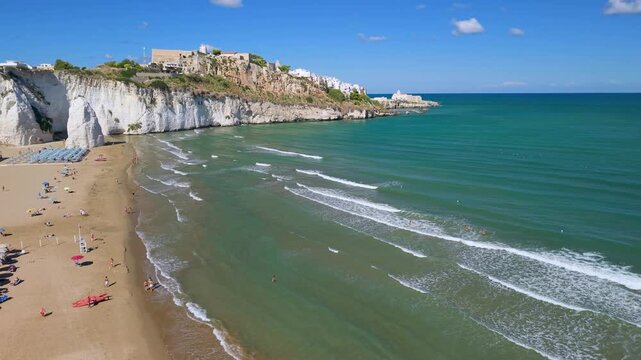 Scenic aerial drone flyover along shoreline beach umbrellas to Pizzomunno monolith in Vieste Italy. Semi circle orbit around giant white sea stack 4K