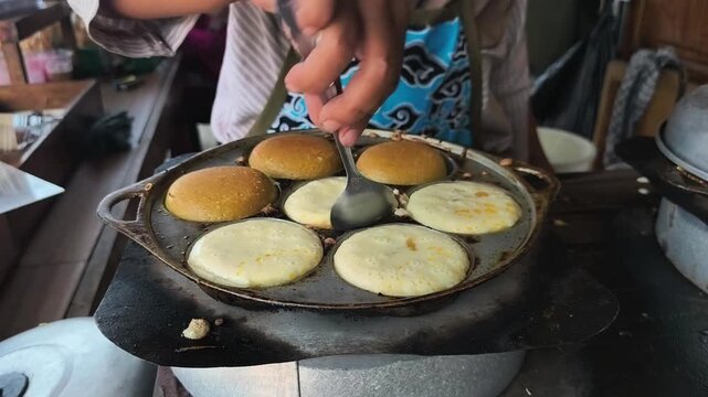 The process of making *Apem* cakes: frying and flipping the cakes in the pan. *Apem* is a traditional Javanese snack made from rice flour.