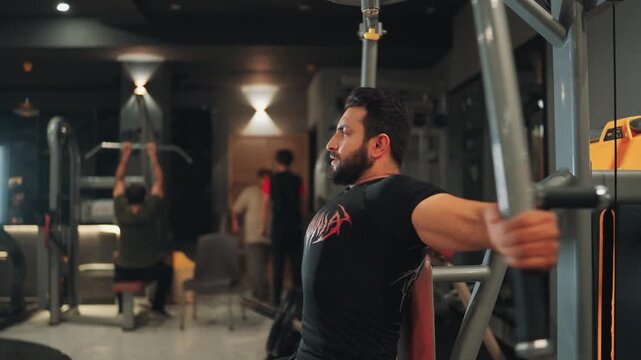 Side view medium shot of a muscular bearded man performing machine chest fly exercises for pectoral muscle isolation and upper body strength in a modern gym.