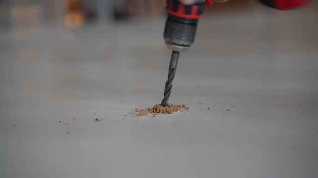 A woodworker is drilling a hole into a white-coated wooden surface using a drill.
