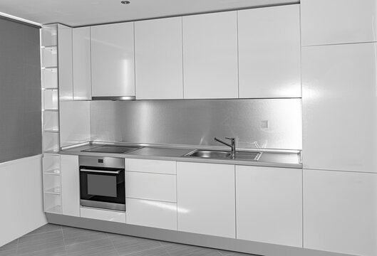 A modern minimalist white kitchen features sleek cabinetry, stainless steel appliances, and a polished backsplash.
