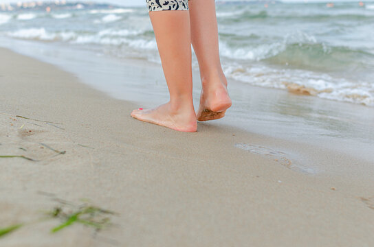 A person walking barefoot on the sandy beach along the sea shore.