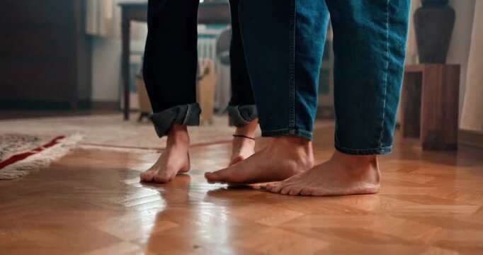 Close-up View of Two People Standing Barefoot on Polished Wooden Parquet Floor in a Cozy Domestic Interior