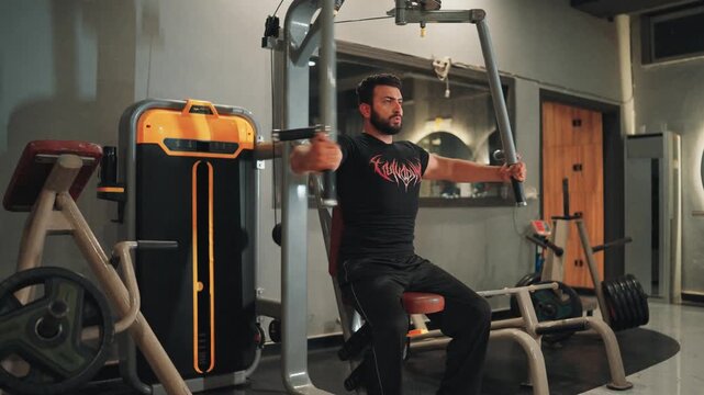 Athletic male athlete executing pec deck machine flyes on selectorized equipment focusing on chest muscle hypertrophy during an indoor workout session.