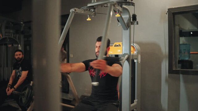 Athletic male athlete stretching pectoral muscles on a seated pec fly machine focusing on chest muscle isolation and upper body workout in a fitness center.