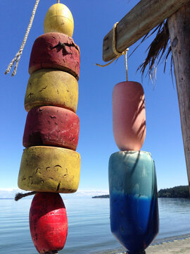 View of colorful fishing floats hanging from a wooden pole against a calm sea and clear blue sky in Victoria, British Columbia, Canada.
