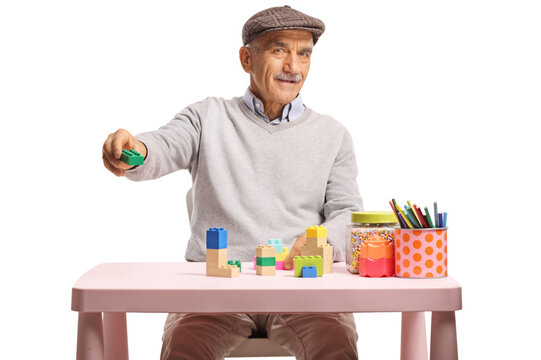 Elderly man sitting at a small table and holding a toy building block