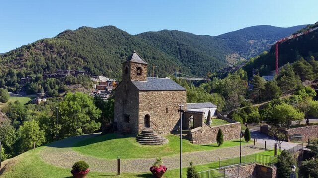 Ancient romanesque stone church of Sant Cristofol d'Anyos in La Massana parish, Andorra, surrounded by green mountains and lush forest under clear blue sky