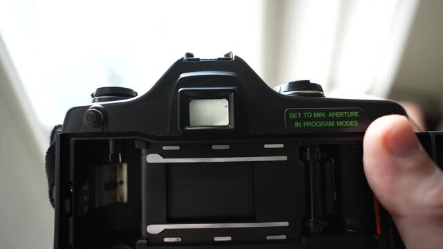 Taking photos inside the house with an analog camera; close-up shots of the camera from a POV perspective, interspersed with views of the camera's internal mechanical details
