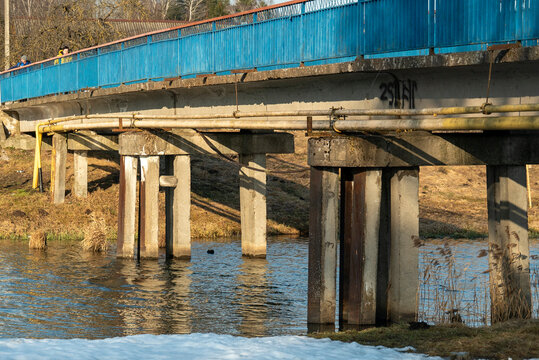 A bridge spans over the water, featuring sturdy support pillars positioned close to the lush grassy bank nearby