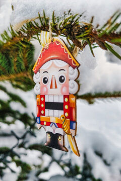 A natural Christmas tree stands in a winter landscape, adorned with a colorful nutcracker ornament. Snow covers the branches, creating a festive scene