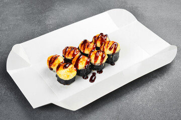 Delicious baked sushi roll set topped with creamy cheese and unagi sauce in takeaway box. Fresh Japanese rolls wrapped in nori. Tasty gourmet food. © Yaruniv-Studio