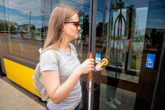 A blind woman with a white cane in her hand and dark glasses boarding the tram