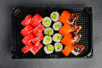 Assorted Japanese sushi rolls topped with fresh salmon shrimp unagi sauce and sesame seeds in takeaway tray. Gourmet seafood set. Tasty fresh Asian food. © Yaruniv-Studio