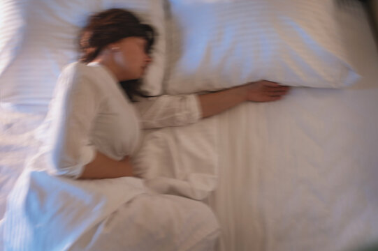 A blurred image of a woman in bed trying to sleep, experiencing menopause symptoms, a drop in estrogen, and depression. Hot flashes, night awakenings. menopausal transition