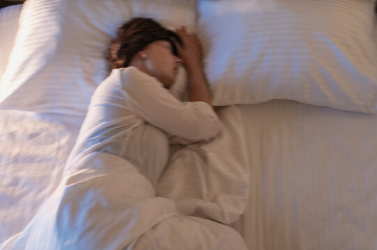 A woman suffering from insomnia in bed. A blurred, out-of-focus photo; symptoms of insomnia, accumulated fatigue and stress, sleep schedule and sleep hygiene.