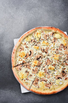 Delicious white pizza with sliced mushrooms, cheese, and dried herbs is placed on a tray. Enjoy the traditional taste of this hot and appetizing meal. Order now.