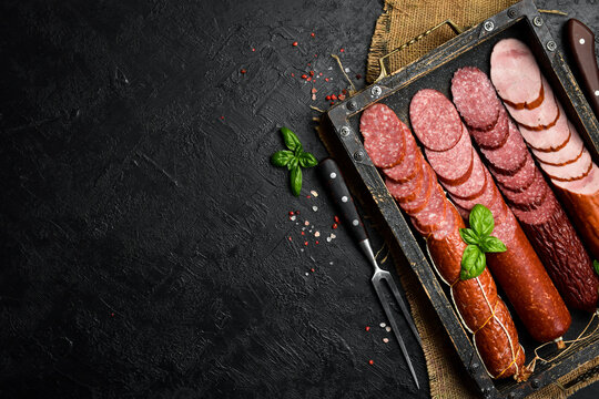 Different types of homemade smoked dry sausages on a dark wooden background. Assortment of delicious deli meats, salami and pepperoni on a tray.