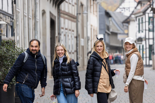 Cheerful friends laugh together on autumn city walk, sharing hugs and joyful travel moments. Candid group portrait captures friendship, reunion, happiness, leisure and weekend adventure outdoors