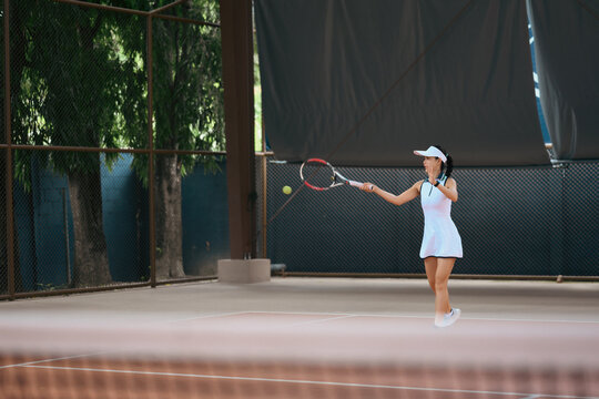Asian Woman Playing Tennis on Outdoor Clay Court in White Sportswear