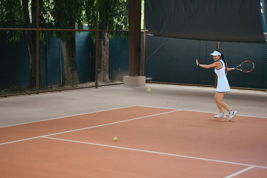 Asian Woman Playing Tennis on Clay Court in White Sportswear Hitting Forehand Shot