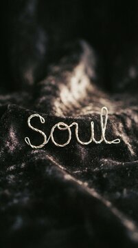 Soul word written in wire script on dark textured fabric with blurred background