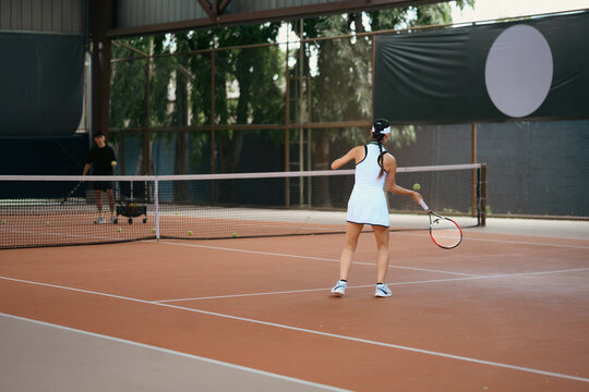 Asian Woman Playing Tennis on Clay Court During Training Session with Coach
