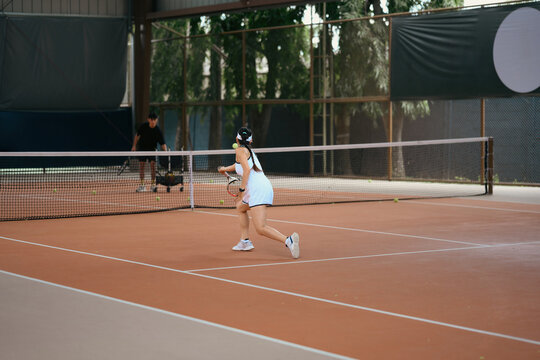 Asian Woman Playing Tennis on Clay Court with Coach or Partner in Background