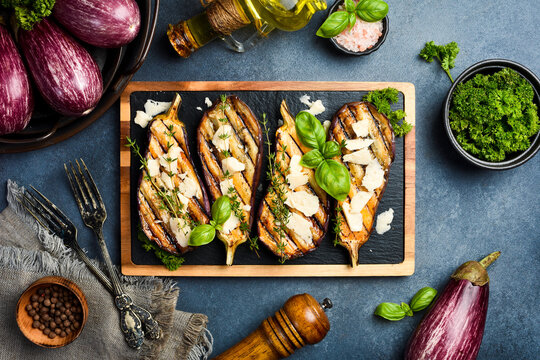 Baked eggplant with cheese and spices on a slate plate. Grilled vegetables. On a gray concrete background.