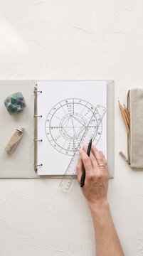 Top view of a hand drawing on an astrological natal chart. Vertical photo of a person analyzing a birth chart with a ruler and pen. Esoteric astrology and horoscope concept