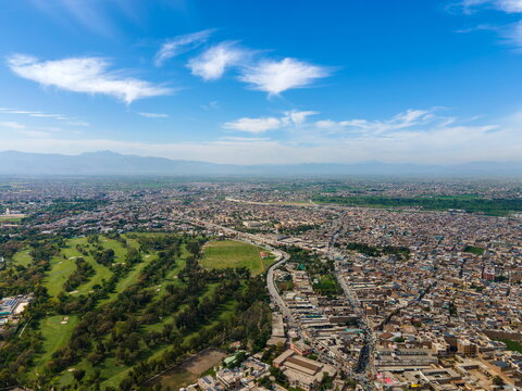 Aerial view of the historic Bala Hisar Fort surrounded by dense urban landscape, green golf course, winding roads, and distant mountains, Peshawar, Khyber Pakhtunkhwa, Pakistan.