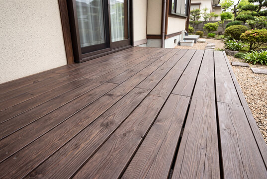 掃き出し窓に面した落ち着いた濃い木色のウッドデッキがある戸建て住宅