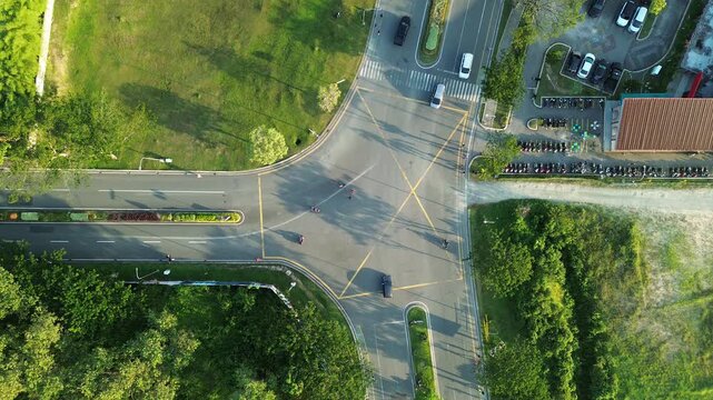 High angle aerial drone view of a road intersection with vehicles driving through a yellow box junction surrounded by lush green landscapes and trees