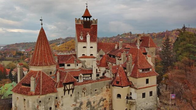 Aerial view of Bran Castle with its iconic red-tiled roofs and stone towers set against the autumn landscape in Bran, Judetul Brasov, Romania.