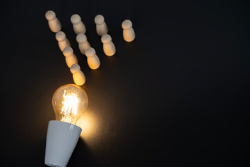 Wooden pegs arranged around a lit bulb on black background © jittawit21
