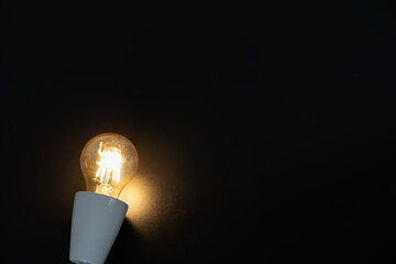 Single incandescent bulb glows warmly in darkness © jittawit21