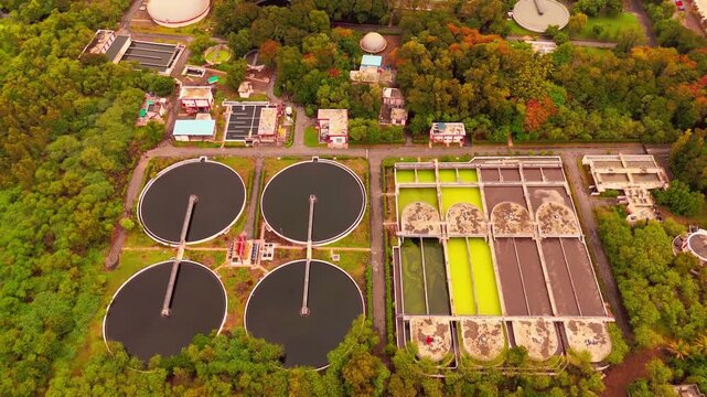 Aerial view of a water treatment facility with circular sedimentation tanks and rectangular filtration basins surrounded by lush green trees in Surat, Gujarat, India.