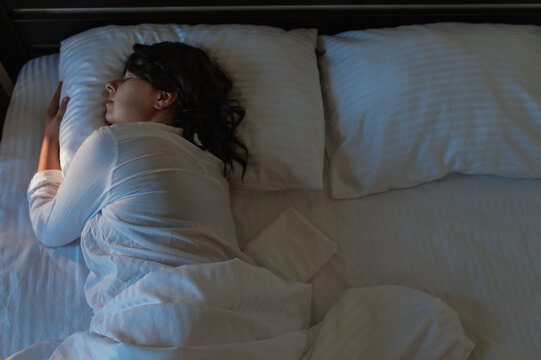 A middle-aged woman with dark hair enjoying a deep, peaceful night's sleep in a cozy home setting.