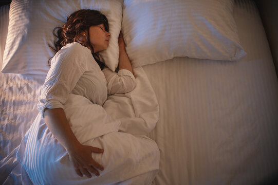 A millennial woman sleeping soundly in her bed at home with a nightlight on; deep sleep, sleep cycles, and melatonin. Sleep hygiene.