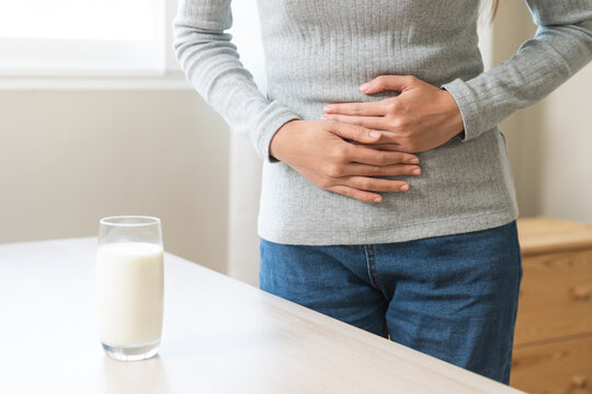 Pain, suffering asian young woman having a stomachache, abdominal pain or digestive, hand in holding belly after drink glass of milk. Lactose intolerance, allergy from dairy food, health care problem.