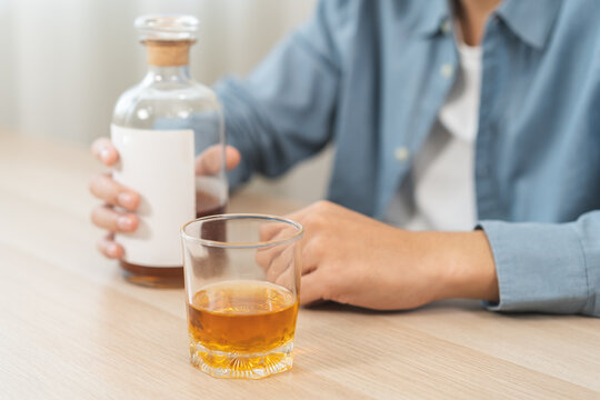 Health care alcoholism drunk, fatigue asian young man hand holding glass bottle of whiskey, depressed male drink booze on table at home. Treatment of alcohol addiction, suffer abuse problem alcoholism