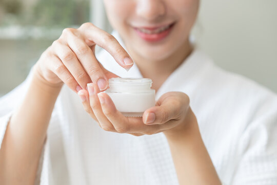 Health care, beauty asian young woman in bathrobe, towel after shower bath, spa relax at home, use finger putting take out moisturizer cream from jar. Skin body moisturizing lotion, routine in morning