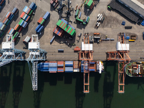 Aerial view of the container terminal with large cranes, colorful shipping containers, and a cargo ship docked in Bajos de Haina, San Cristobal Province, Dominican Republic.