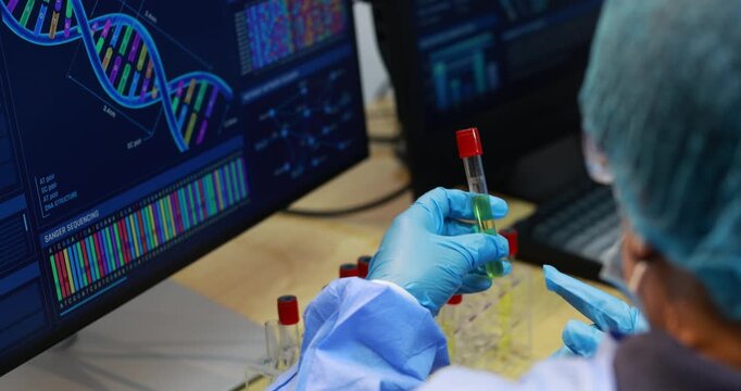 Scientists in a laboratory examine a sample vial while viewing dna sequence data and genetic charts on computer screens.