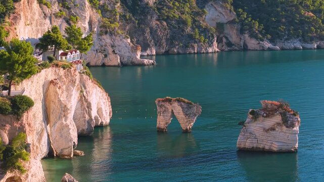Baia delle Zagare sunrise aerial 70mm view Faraglioni sea stacks in pink morning light Gargano Puglia Italy iconic empty beach with turquoise Adriatic Sea and pine trees cinematic B-roll