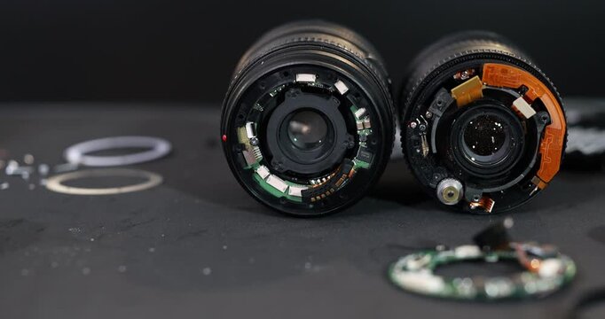Close-up of two disassembled camera lenses exposed electronic parts, circuit boards, glass elements, and small components on a dark work surface.