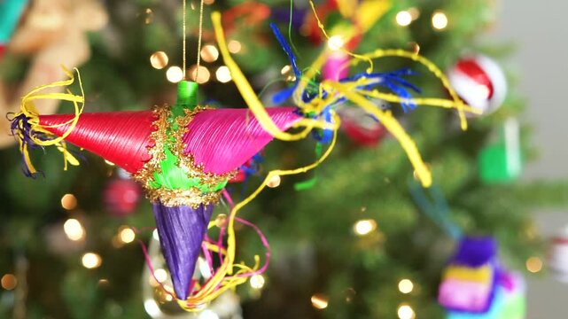 Colorful pinata hangs before a twinkling tree. Festive tinsel swirls around the pinata's bright form. Joyful lights glow behind the decorated holiday tree. Perfect for fiesta or party themed videos