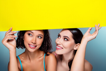 Two smiling women hold a bright yellow sign above their heads during a friendly fashion and beauty photo shoot © Beauty Hero